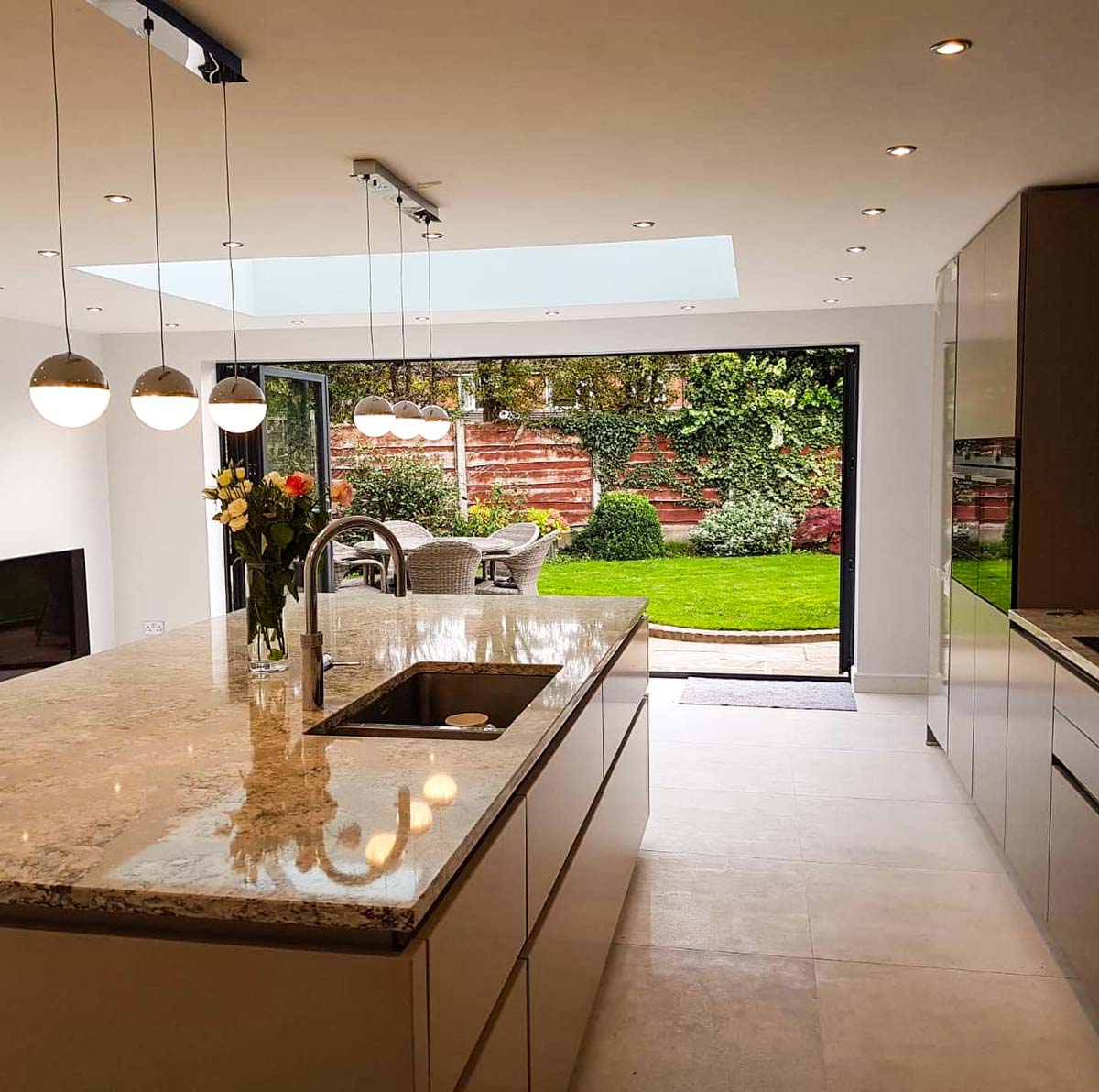 External view of a contemporary flat-roof rear kitchen extension with roof lanterns and sleek bifold doors.